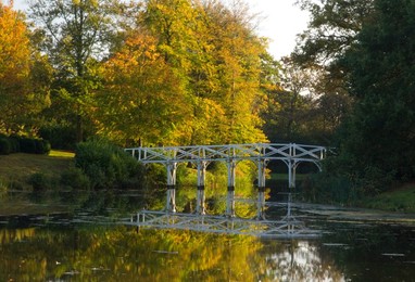 A wooden bridge across the lake at Painshill Landscape Garden in autumn, Cobham, Surrey, England, United Kingdom, Europe