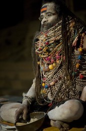 Lali Baba, a priest waiting for worshippers that he will bless with ash from the bowl at his feet, wearing necklaces given to him to worship Shiva, Varanasi, Uttar Pradesh, India, Asia