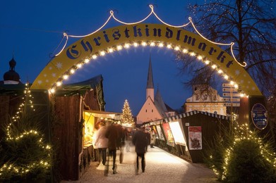 Sign over gate and stalls, Christmas Market (Christkindlmarkt) on Kapellplatz Square, at twilight, Altotting, Bavaria, Germany, Europe