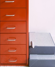 Modern, red, six drawer filing cabinet next to stacked grey magazine storage box