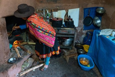 Local woman in colourful traditional dress cooks breakfast over an open fire, Chumbe Community, Lamay, Sacred Valley, Peru, South America