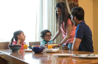 Mother serving food to family at dining table in house