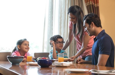 Woman serving food to family at dining table in house