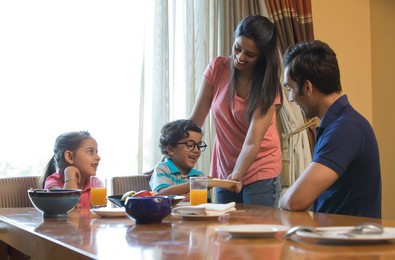 Woman serving food to family at dining table in house