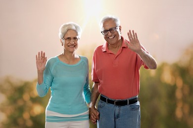 Smiling senior couple standing outdoors in nature and waving hands