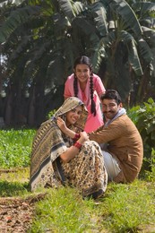 Happy and smiling rural family sitting in their agriculture field.