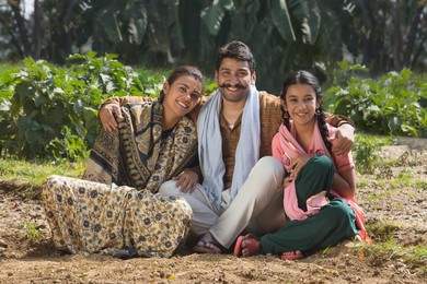 Happy and smiling rural family sitting in their agriculture field.