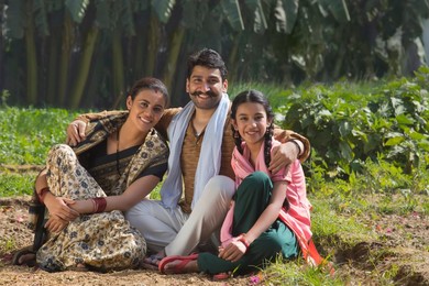 Happy and smiling rural family sitting in their agriculture field.