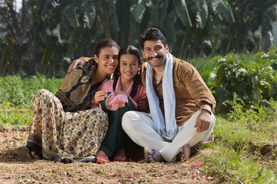 Happy and smiling rural family sitting in their agriculture field.