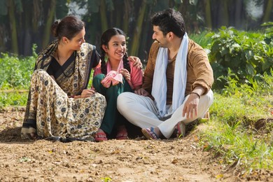 Happy and smiling rural family sitting in their agriculture field.