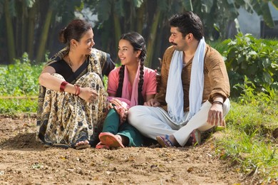 Happy and smiling rural family sitting in their agriculture field.