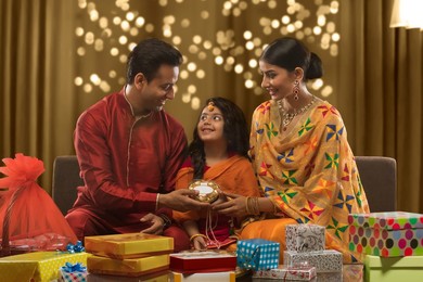Happy family sitting on a sofa holding presents on diwali