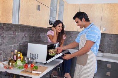 Happy woman looking at man preparing food in kitchen