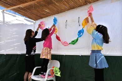 Jewish family decorating the interior of a Sukkah with colourful traditional  artwork