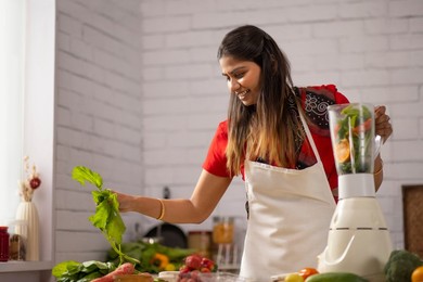 Portrait of smiling woman preparing healthy smoothie in kitchen