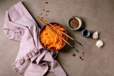 Dish of the rean and Asian Cuisine: Vegetable Salad Marinated Carrots with Garlic. Served In Ceramic Bowl with Chopsticks. Seasoning In Small Bowls on Mocha Mousse Tones Table. Healthy Eating. Top View