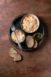 Traditional Appetizer Sauerkraut Cabbage with Carrots In Bowl and Jar. Sea Salt. Olive Oil. Sliced Rye Bread. and Fork Nearby. Healthy Food. Fermented Products. Brown Textured Background. Top View.