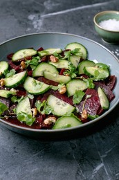 Vegan Beet Salad. Marinated Sliced Beetroot With Fresh Cucumber. Walnuts. and Coriander Leaves In Ceramic Bowl. Nearby Bowl With Sea Salt On Black Marble Table. Vibrant. Healthy. Plant-based Dish.