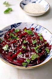 Korean-style Beet Salad. Marinated Grated Beetroot With Sesame Seeds and Coriander Leaves In Ceramic Bowl. Nearby Bowl With Sesame Seeds On White Marble Table. Vegan Healthy Dish. Close Up