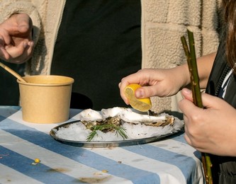 Street Food Festival Europe. Woman Squeezing Lemon Over Fresh Oysters On Ice Plate. Traditional Seafood Delicacy Served Outdoor Table. Gourmet Street Cuisine Experience