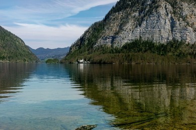 Hallstatt Austria. Serene Alpine Lake Surrounded by Steep Mountain Ranges Reflecting In Clear Turquoise Water. Small Settlement Visible At Shoreline. Landscape Nature Scene For Travel Destination