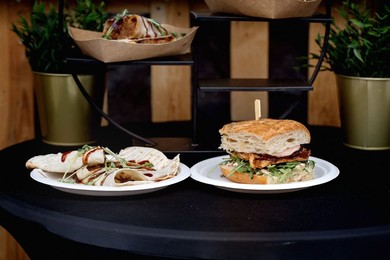 Delicious Street Food Sandwich with Meat Arugula on Plate Next to Wrapped Tortilla. Ecofriendly Packaging Visible In Background with Decorative Plants Stylish Food Presentation