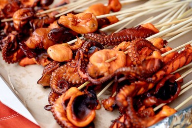 Closeup of Grilled Baby Octopus on Wooden Skewers. Seafood Barbecue with Charred Octopus Pieces Showcasing Tentacles Texture. Mediterranean Cuisine Street Food