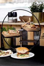 Stylish Tiered Food Display Stand with Gourmet Sandwiches In Kraft Paper Containers And White Plate. Modern Restaurant Presentation with Herbs And Spices In Background