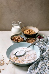 Homemade Sprouted Wheat Breakfast Setup with Bowl of Milk Cereals Walnuts Dried Berries. Healthy Morning Meal Ingredients on White Table with Floral Cloth